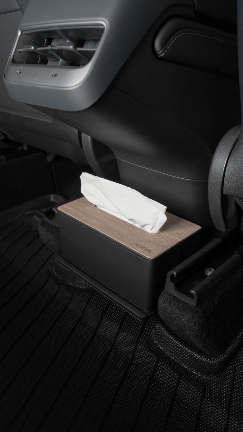 A JOWUA tissue box holder with a wooden top is placed on the All Model Y All-Weather Floor Liners from JOWUA in the backseat area of a Tesla Model Y, positioned between the rear seats, just in front of the center console’s air vents, atop a durable rubber mat.
