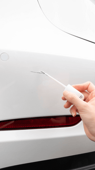 A hand uses an ultra-thin brush from the JOWUA Touch-up Paint for Tesla Model S/3/X/Y (2 pieces) to skillfully apply white paint, effectively covering chips on a Tesla