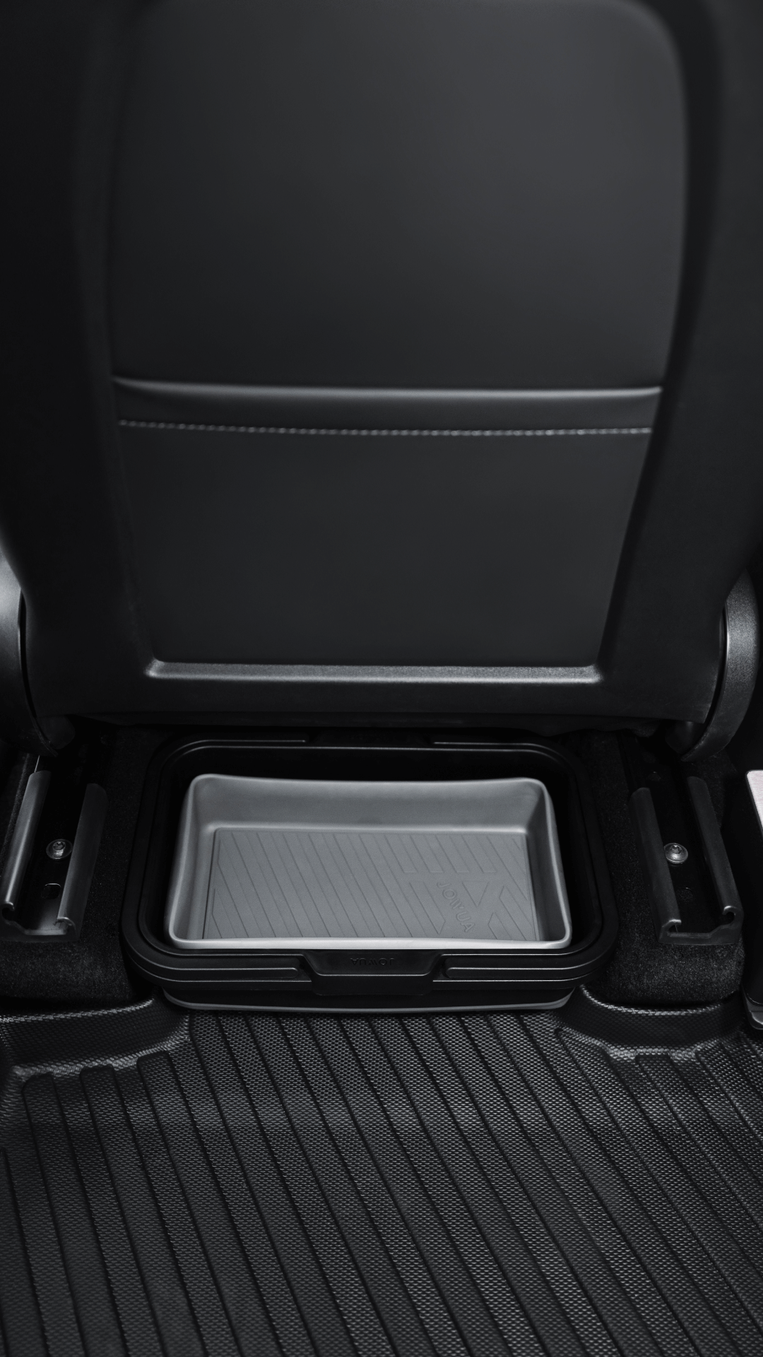 A close-up of the JOWUA Under Seat Collapsible Organizer (Set of 2) for Tesla Model X Y placed under the rear seat, with black rubber floor mats and the back of a front seat visible.