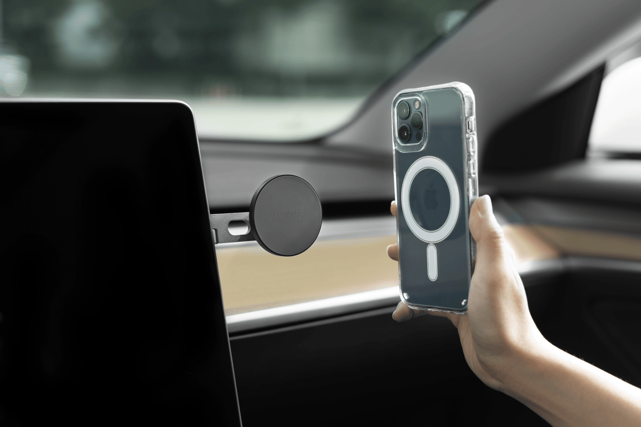 A hand holding an iPhone encased in a JOWUA iPhone Case for Tesla Model Y/3 Mount - MagSafe (iPhone 11/12 Series) hovers near the MagSafe Car Mount inside the elegant interior of a Tesla Model 3. The car boasts a digital display, seamlessly blending technology and style for an effortless driving experience.