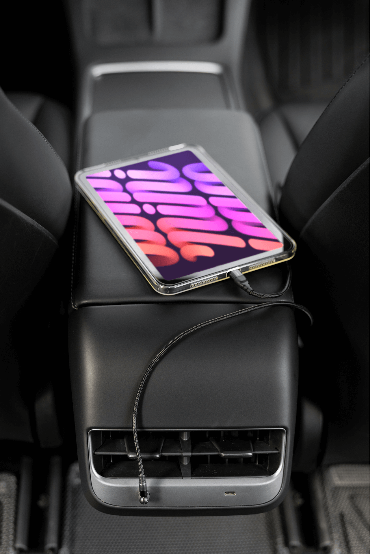 A tablet showcasing a vibrant, colorful abstract pattern rests on the armrest of a Tesla Model 3. It's seamlessly connected using the JOWUA Magnetic Charging Cable USB-C to USB-C (1M-1.8M), plugged in below the armrest. The car's sleek interior, including seats and airflow vents, completes this tech-savvy setup.