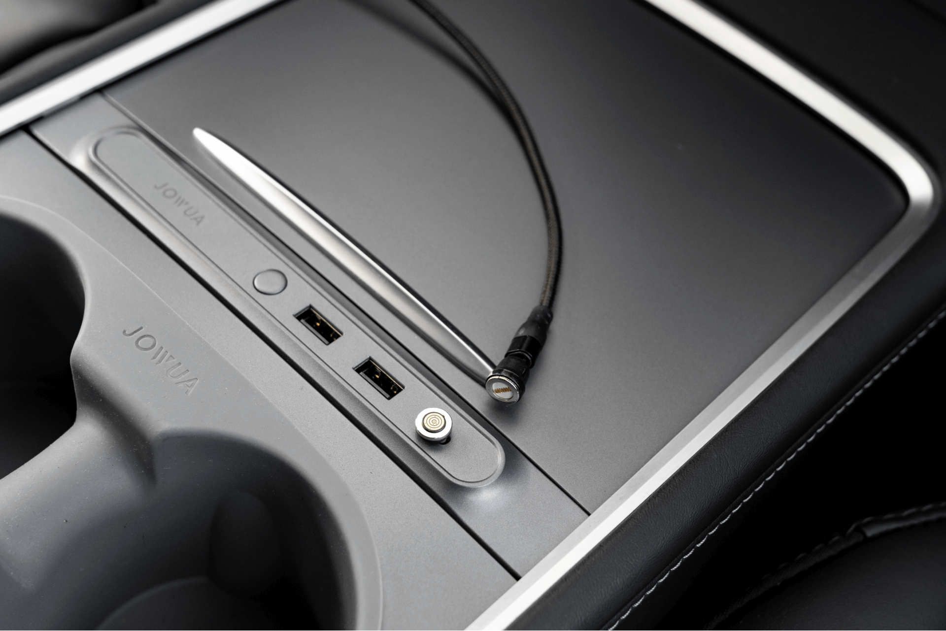 The center console, perfect for Tesla Model 3 accessories, includes a JOWUA Magnetic Charging Cable USB-C to USB-C that extends from 1M to 1.8M alongside two USB ports and a covered receptacle with a sleek metallic finish. It offers easy use with its magnetic cable connector and features a visible cup holder on the left.
