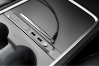 The center console, perfect for Tesla Model 3 accessories, includes a JOWUA Magnetic Charging Cable USB-C to USB-C that extends from 1M to 1.8M alongside two USB ports and a covered receptacle with a sleek metallic finish. It offers easy use with its magnetic cable connector and features a visible cup holder on the left.