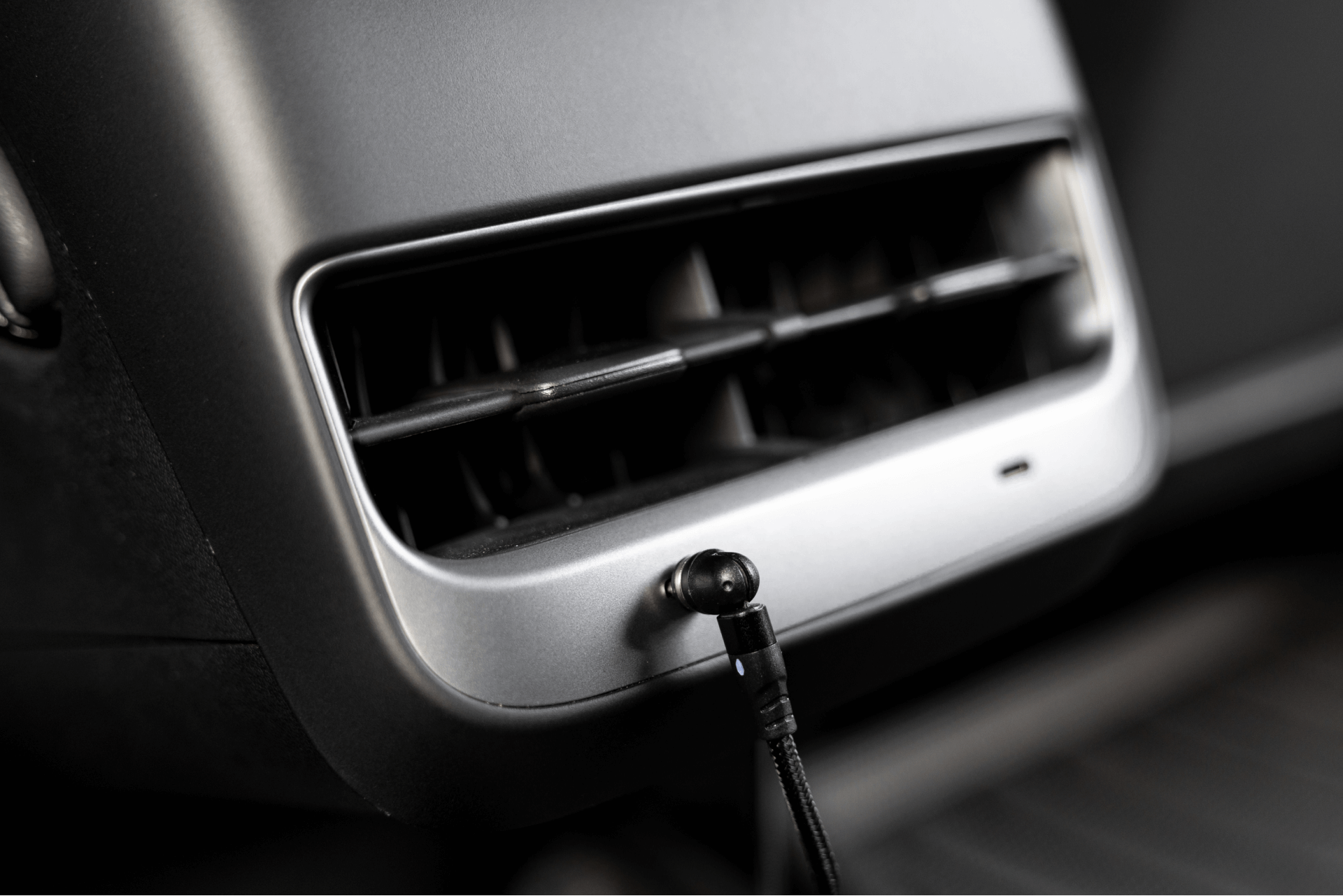 A close-up of a Tesla Model 3 interior reveals an air vent with a JOWUA Magnetic Charging Cable USB-C to USB-C (1M-1.8M) neatly plugged into a port below. The sleek black and grey color scheme enhances the modern design, showcasing an accessory that ensures fast charging convenience on the go.