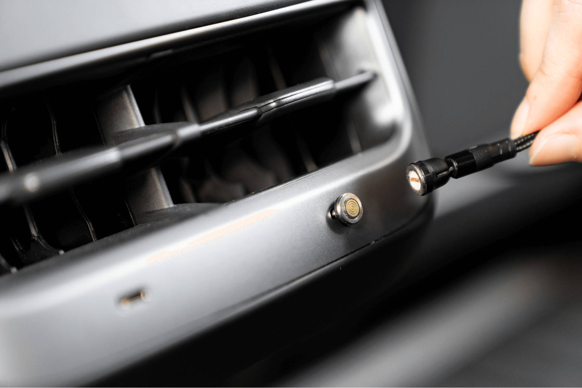 A hand holding a JOWUA Magnetic Charging Cable USB-C to USB-C (1M-1.8M) is about to connect it to a round socket on a device panel near an air vent. The image captures the precise action of plugging in, highlighting the socket and sleek design of the connector, reminiscent of Tesla Model 3 accessories.