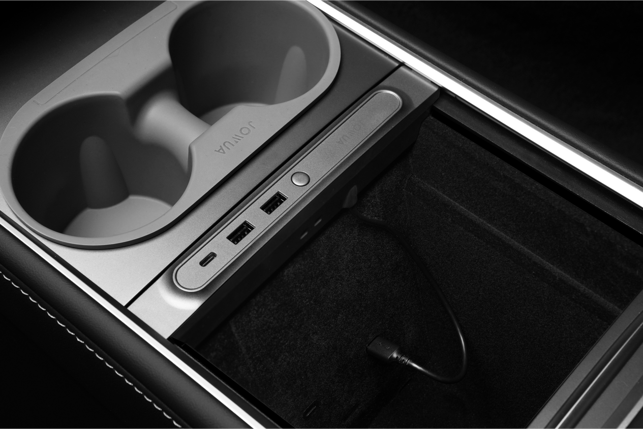 A close-up of a car interior showcases a center console with two cup holders, a storage compartment, and USB ports. A JOWUA 36W Hub Charging Combo powers the dashcam via cable. Elegantly framed by LED lighting, "JOULE" stands out on the panel.