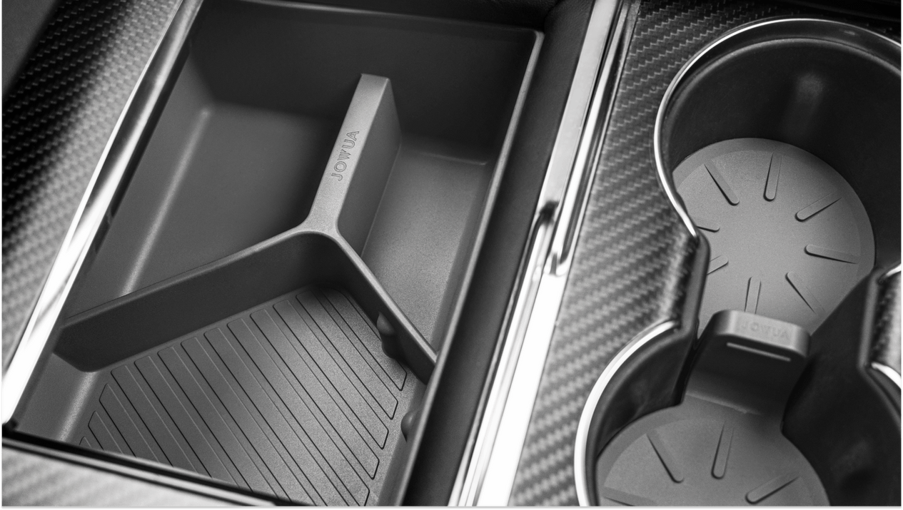 Close-up of a Tesla Model S center console featuring the JOWUA Center Console Set, which includes a premium silicone organizer with divided storage compartments on the left, showcasing vertical ridges, along with two cup holders on the right. The sleek, modern design is enhanced by a carbon fiber texture surrounding the compartments.