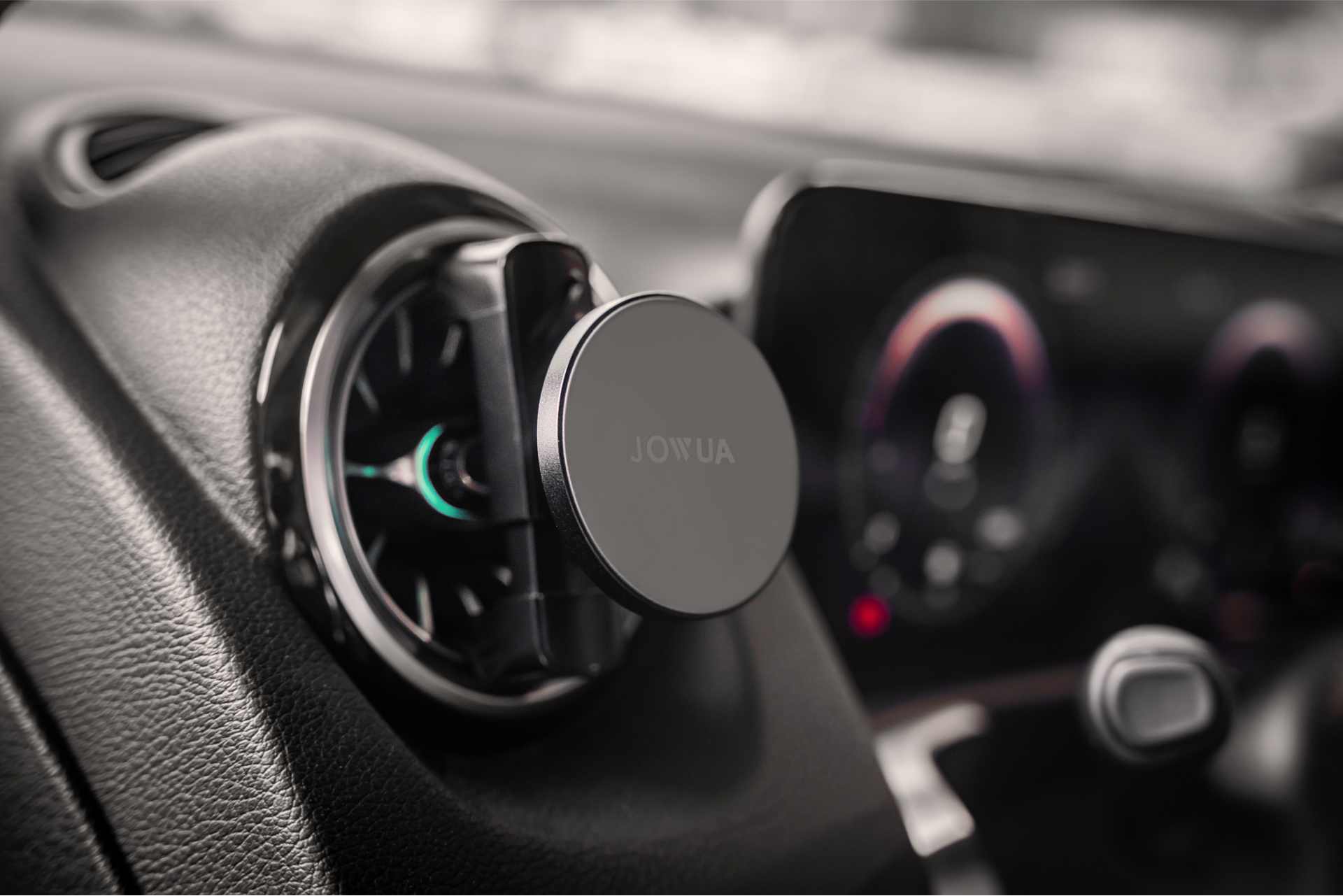 A car interior displaying a JOWUA Universal MagSafe Car Mount for Air Vents, highlighting its MagSafe compatibility. In the background, the dashboard and part of the infotainment system with lit-up dials are visible.