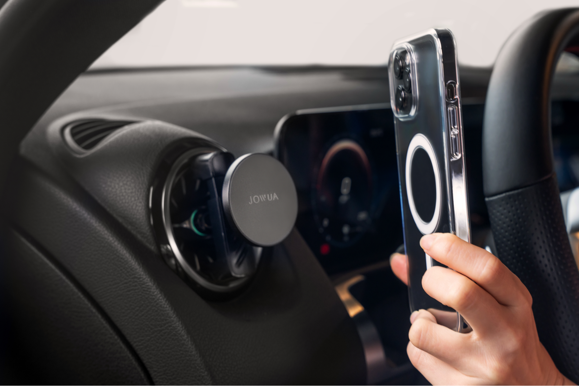 In a vehicle, a smartphone is placed in front of the JOWUA Universal MagSafe Car Mount for Air Vents. This mount accommodates MagSafe-compatible accessories, and the phone, equipped with a circular magnetic ring, is prepared for 15W fast charging.