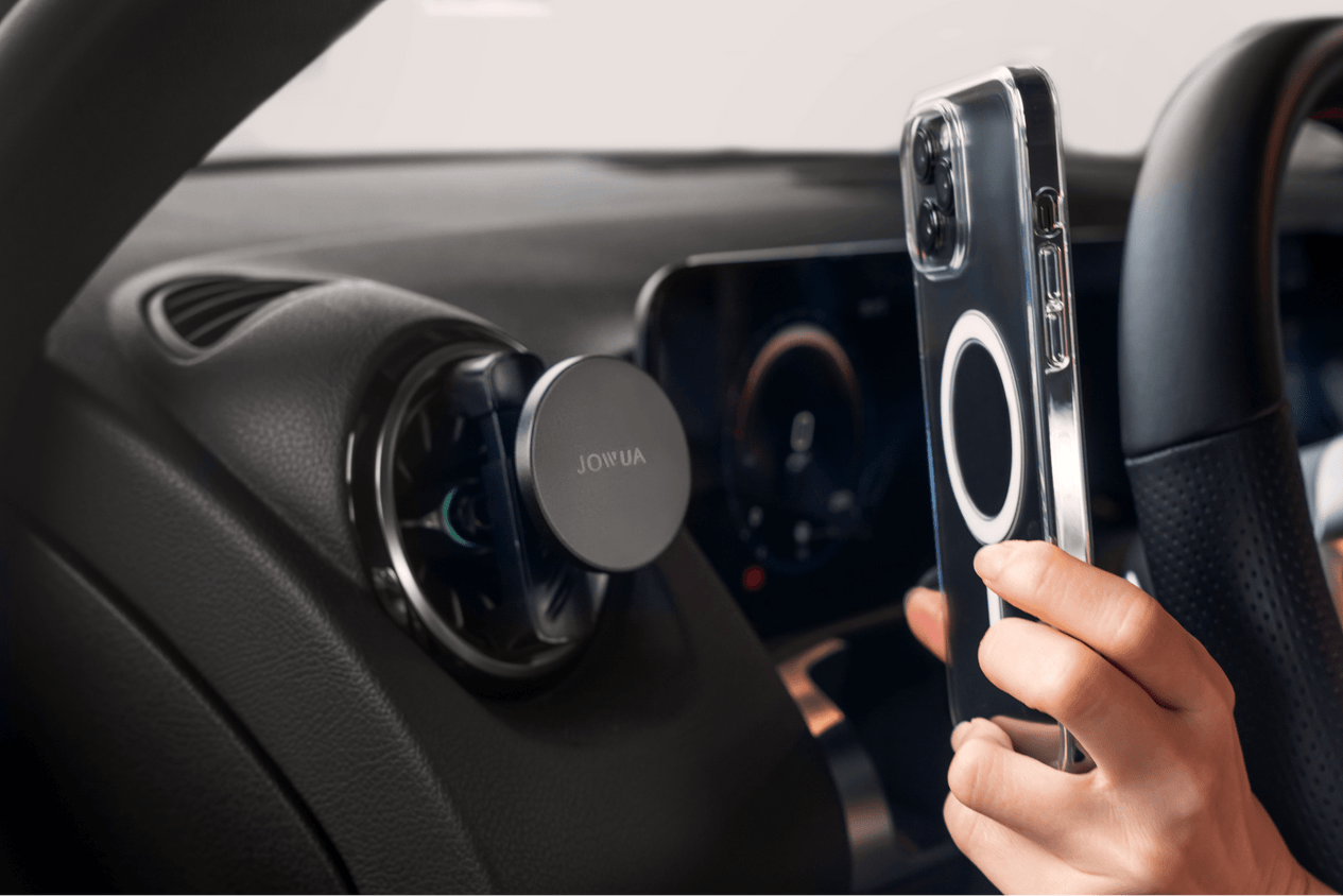 In a vehicle, a smartphone is placed in front of the JOWUA Universal MagSafe Car Mount for Air Vents. This mount accommodates MagSafe-compatible accessories, and the phone, equipped with a circular magnetic ring, is prepared for 15W fast charging.
