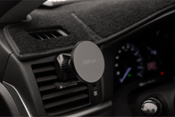 The image showcases a close-up of a car dashboard with the JOWUA Universal MagSafe Car Mount clipped onto an air vent, providing Qi2 Wireless Charging. The speedometer and other dashboard controls are slightly blurred in the background, keeping your device powered while on the move.