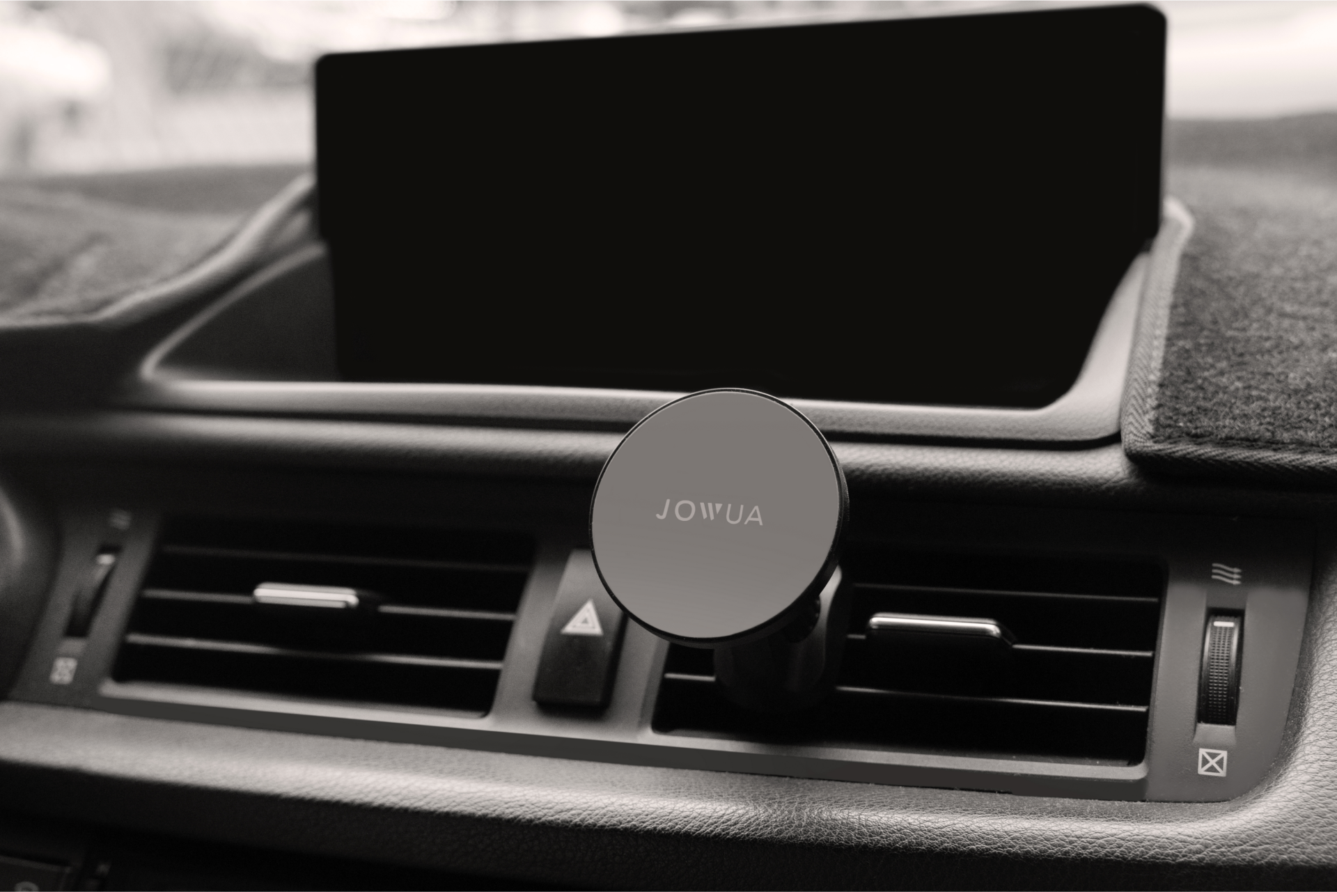 The dashboard features a JOWUA Universal MagSafe Car Mount for Air Vents with 360° rotation positioned on the air vent. Above the air vent controls is an unlit screen, and the color scheme throughout is black and gray.
