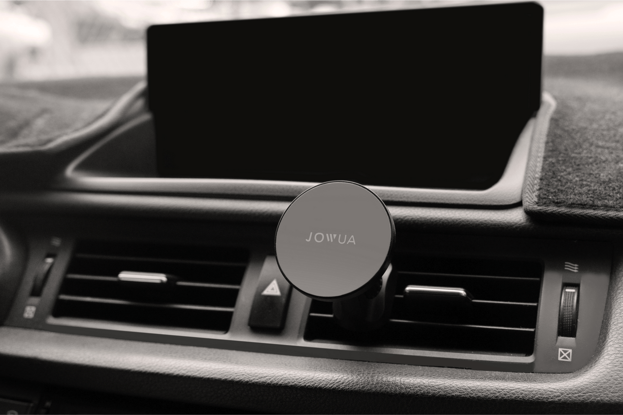 The dashboard features a JOWUA Universal MagSafe Car Mount for Air Vents with 360° rotation positioned on the air vent. Above the air vent controls is an unlit screen, and the color scheme throughout is black and gray.