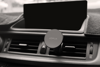 The dashboard features a JOWUA Universal MagSafe Car Mount for Air Vents with 360° rotation positioned on the air vent. Above the air vent controls is an unlit screen, and the color scheme throughout is black and gray.
