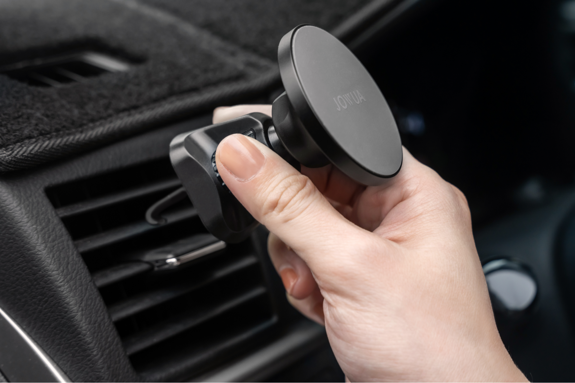 A person adjusts a JOWUA Universal MagSafe Car Mount for Air Vents, which features 360° rotation. The mount is round and black, keeping your device perfectly positioned for every journey.